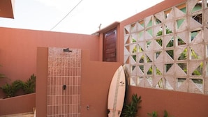 A gated entrance with a tiled gate, a surfboard leaning against a wall, and a window with a geometric pattern. - Kali House (Tibau do Sul)