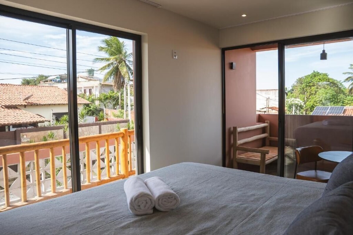 A hotel room with a bed, a balcony with a view of the neighborhood, and a table with chairs.