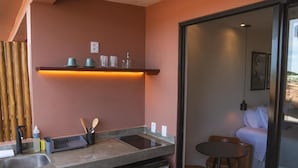 A compact kitchen with a built-in dishwasher, a small dining area with a table and chairs, and a glass door leading to a bedroom. - Kali House (Tibau do Sul)