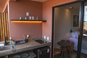 Una cocina compacta con lavavajillas integrado, un pequeño comedor con mesa y sillas, y una puerta de cristal que da a un dormitorio.