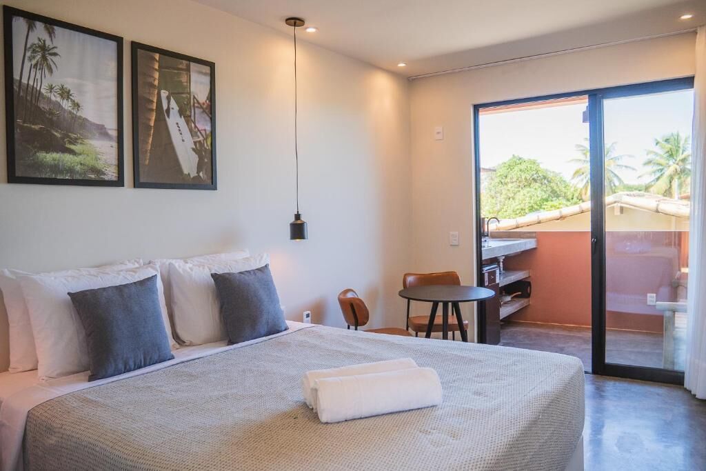A hotel room with a bed, a desk, a chair, and a sliding glass door leading to a balcony.
