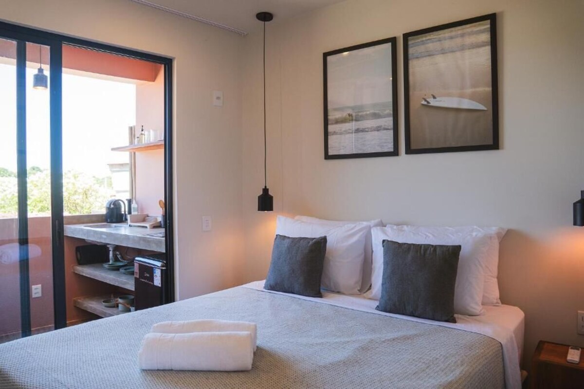 A bedroom with a bed, pillows, a nightstand, a wall-mounted lamp, and two framed pictures.