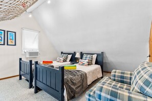 Ein Schlafzimmer mit Etagenbett, Einzelbett, Schreibtisch, Stuhl, einer Hängematte und einem Fenster mit Jalousien.