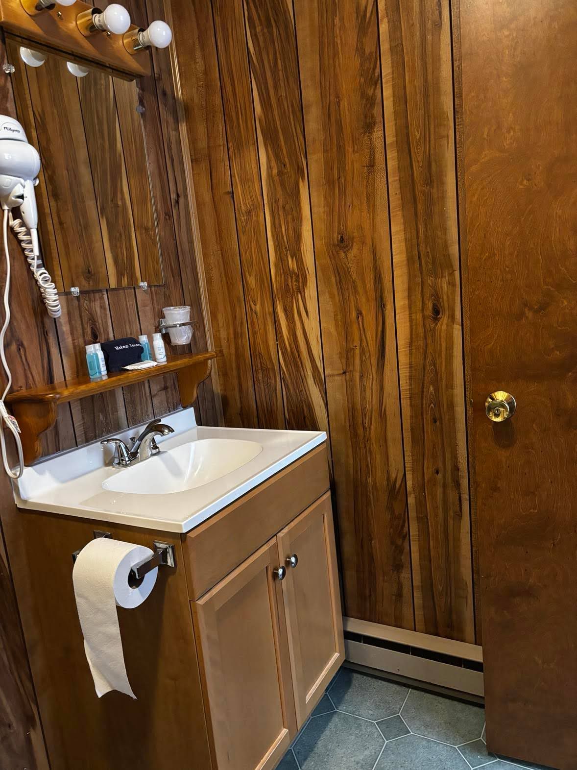 Un baño de madera con lavamanos, espejo y artículos de tocador.