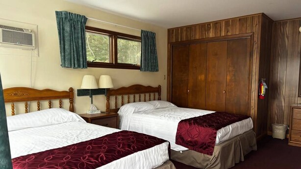 Een kamer met twee bedden, een houten garderobe, een raam met gordijnen, een lamp en een brandblusser.