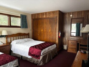 A bedroom with a wooden wardrobe, a bed with a red and white bedspread, a bedside table with a lamp, and a window with curtains. - Cozy 1-bedroom hotel room, Hamilton - 314 Gilbreth (Hamilton)