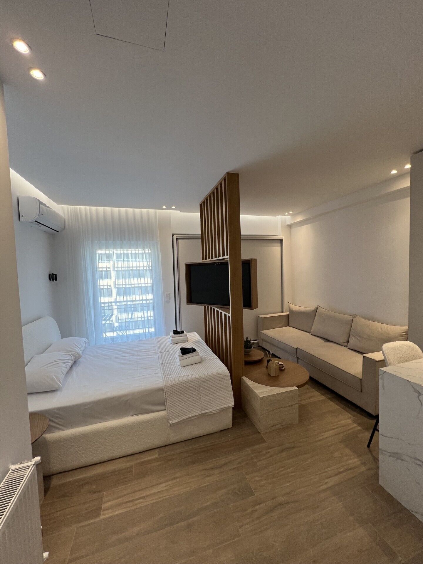 A modern hotel room with a bed, a sofa, a TV, and a window with curtains.