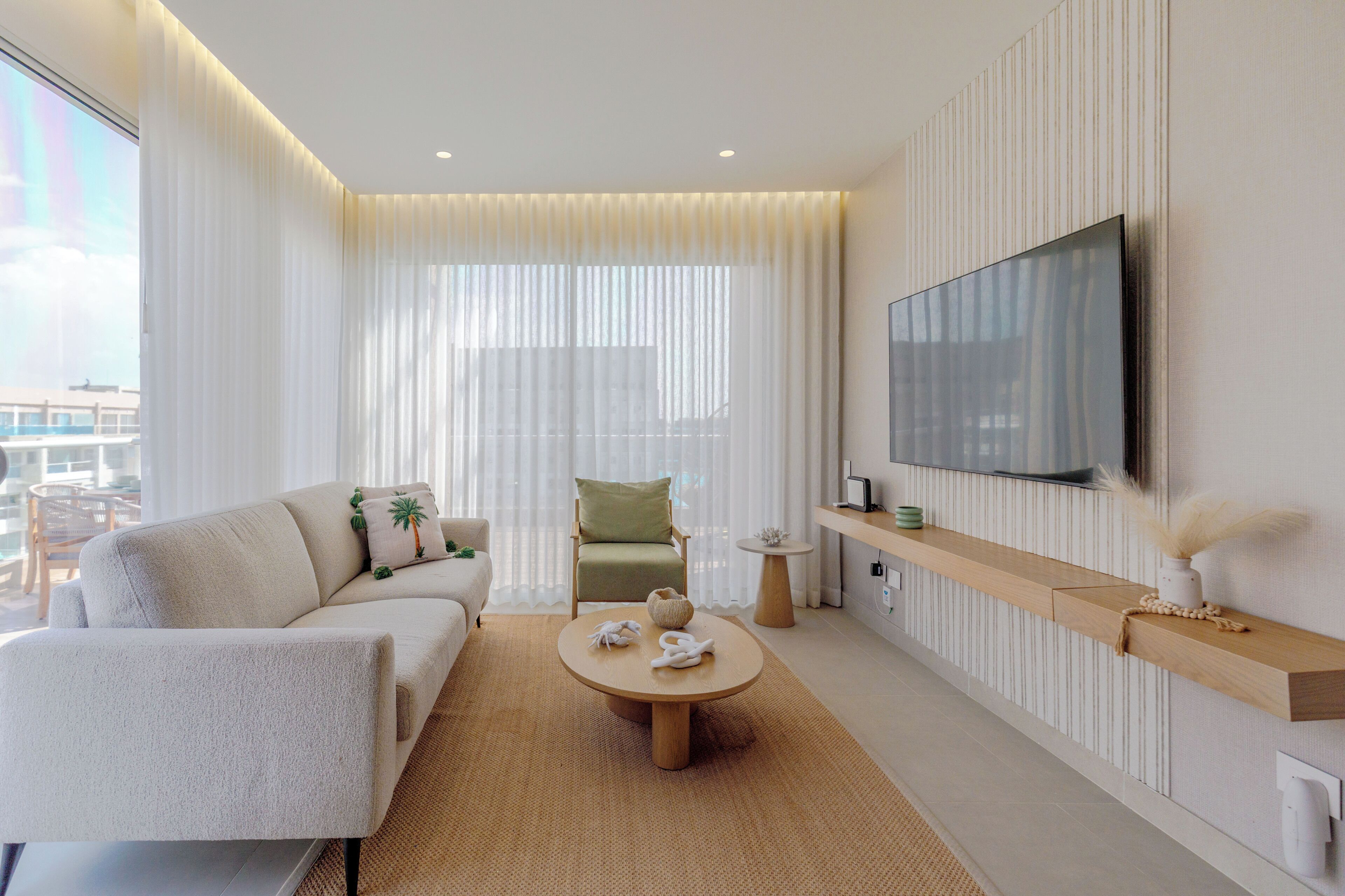 Un salon moderne comprenant un canapé, un fauteuil, une table basse ronde et un téléviseur fixé au mur.