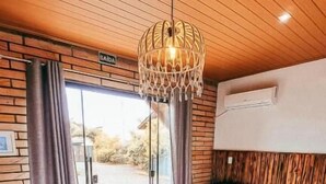 Hotellihuone, jossa on puinen katto, kuviollinen peitto sängyllä, riippuvalaisin ja näkymä lasiovesta.