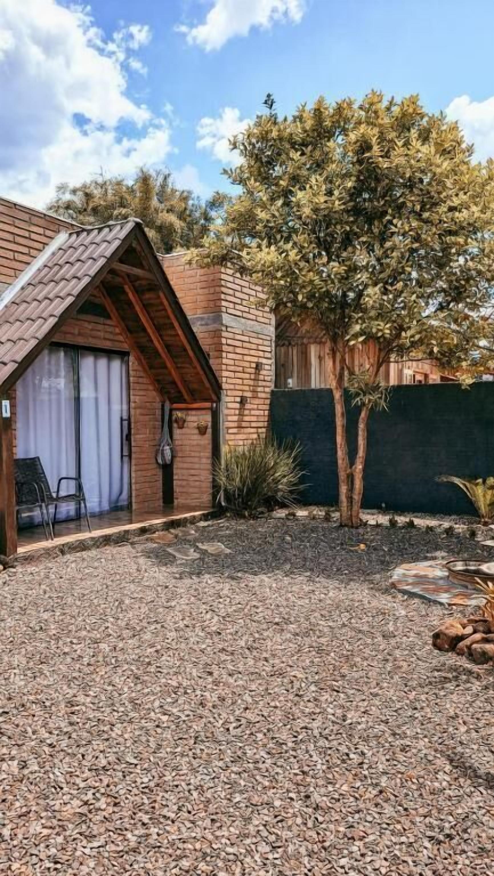 Une petite maison en briques avec un toit en pente, une terrasse avec un sol en gravier et un arbre.