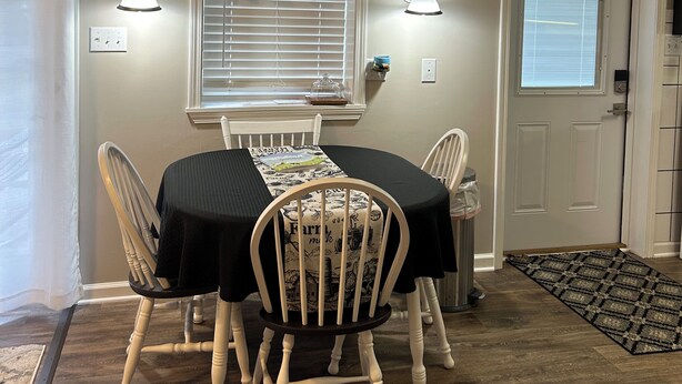A dining area with a table, chairs, a window with blinds, wall-mounted lights, and a door with a window.