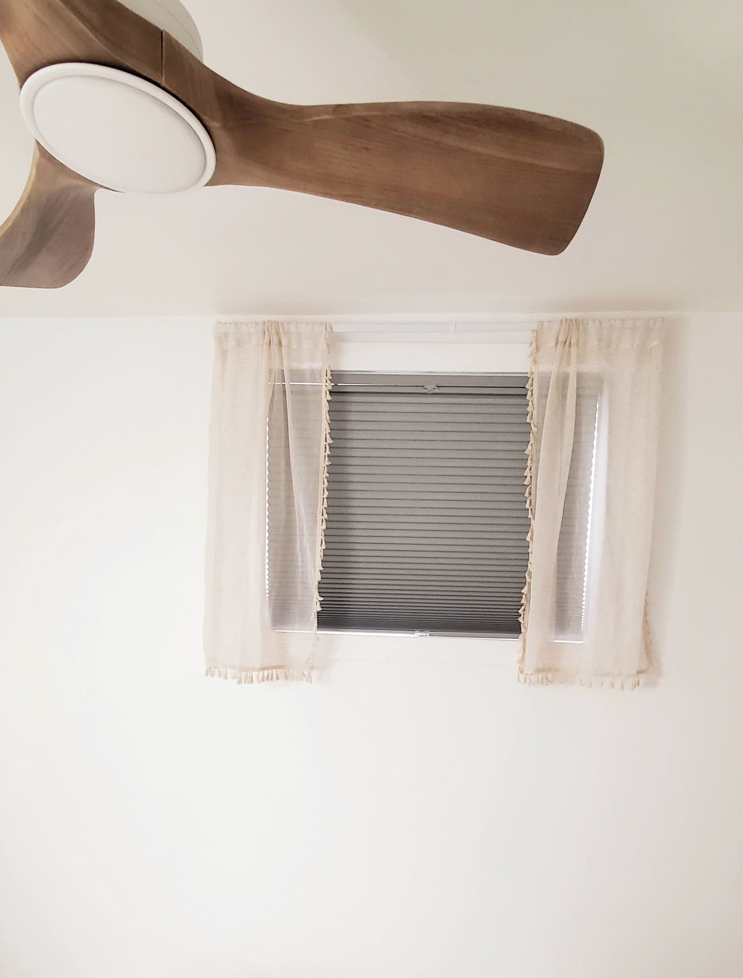 A ceiling fan, a window with blinds, and a wall.