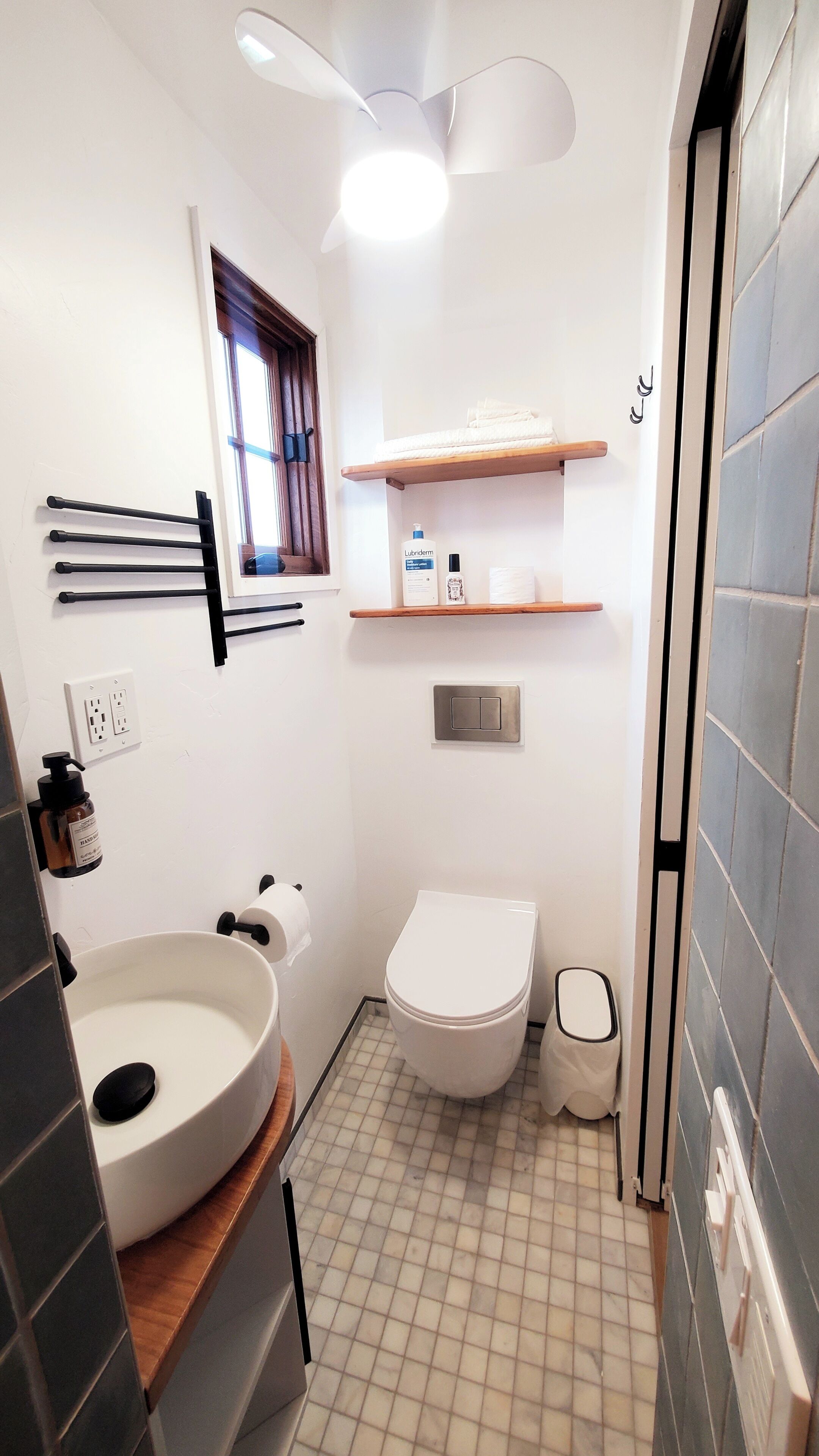 Een badkamer met toilet, wastafel, handdoekrek, planken met toiletartikelen en een raam.