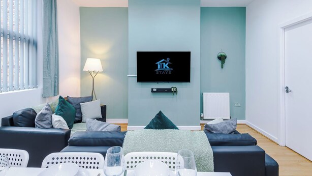 Uma sala de estar moderna com sofá, televisão de tela plana, luminária e área de jantar com cadeiras e mesa.
