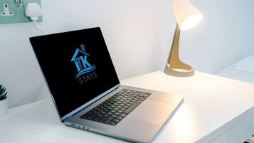 Ein Laptop auf einem weißen Schreibtisch, mit einem Logo auf dem Bildschirm, einer Lampe und einer Steckdose.