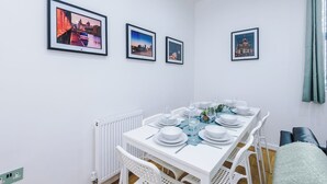 Uma sala de jantar com uma mesa branca posta para quatro pessoas, quadros com vista da cidade nas paredes e um radiador branco.