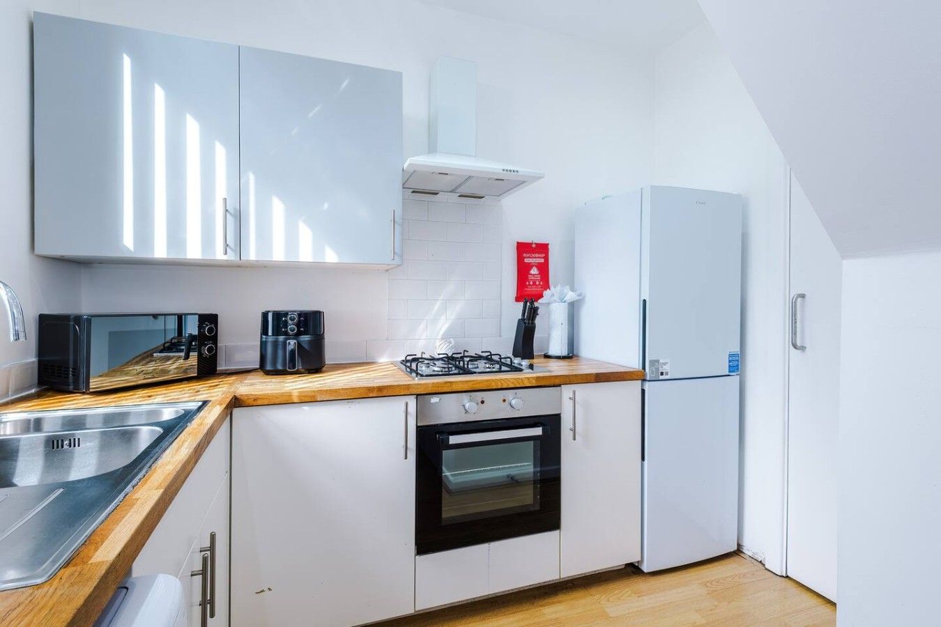 Eine moderne Küche mit weißen Schränken, einer Holzausziehtafel, einem Gasherd, einer Mikrowelle und einem Kühlschrank.