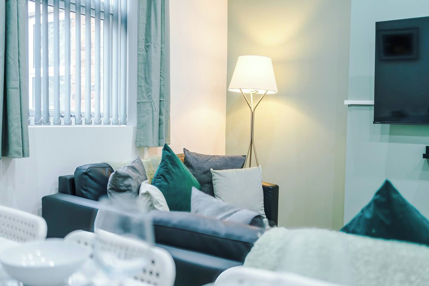 Ein modernes Wohnzimmer mit einer Couch, Kissen, einer Lampe und einem an der Wand befestigten Fernseher.