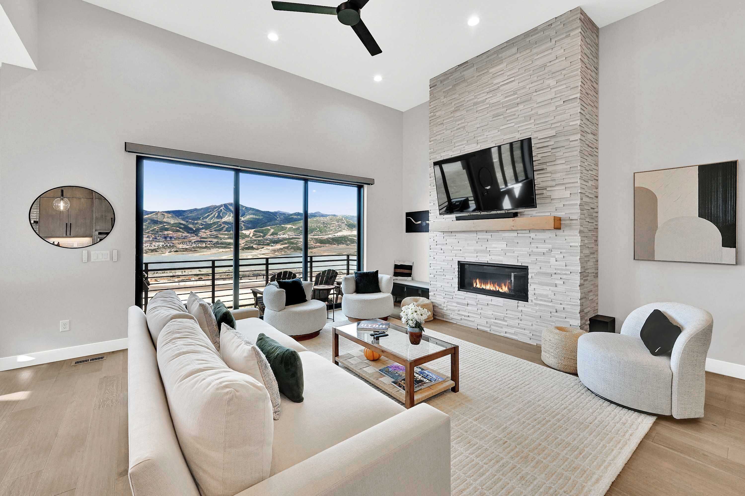A modern living room with a fireplace, large windows, and a view of a mountainous landscape.