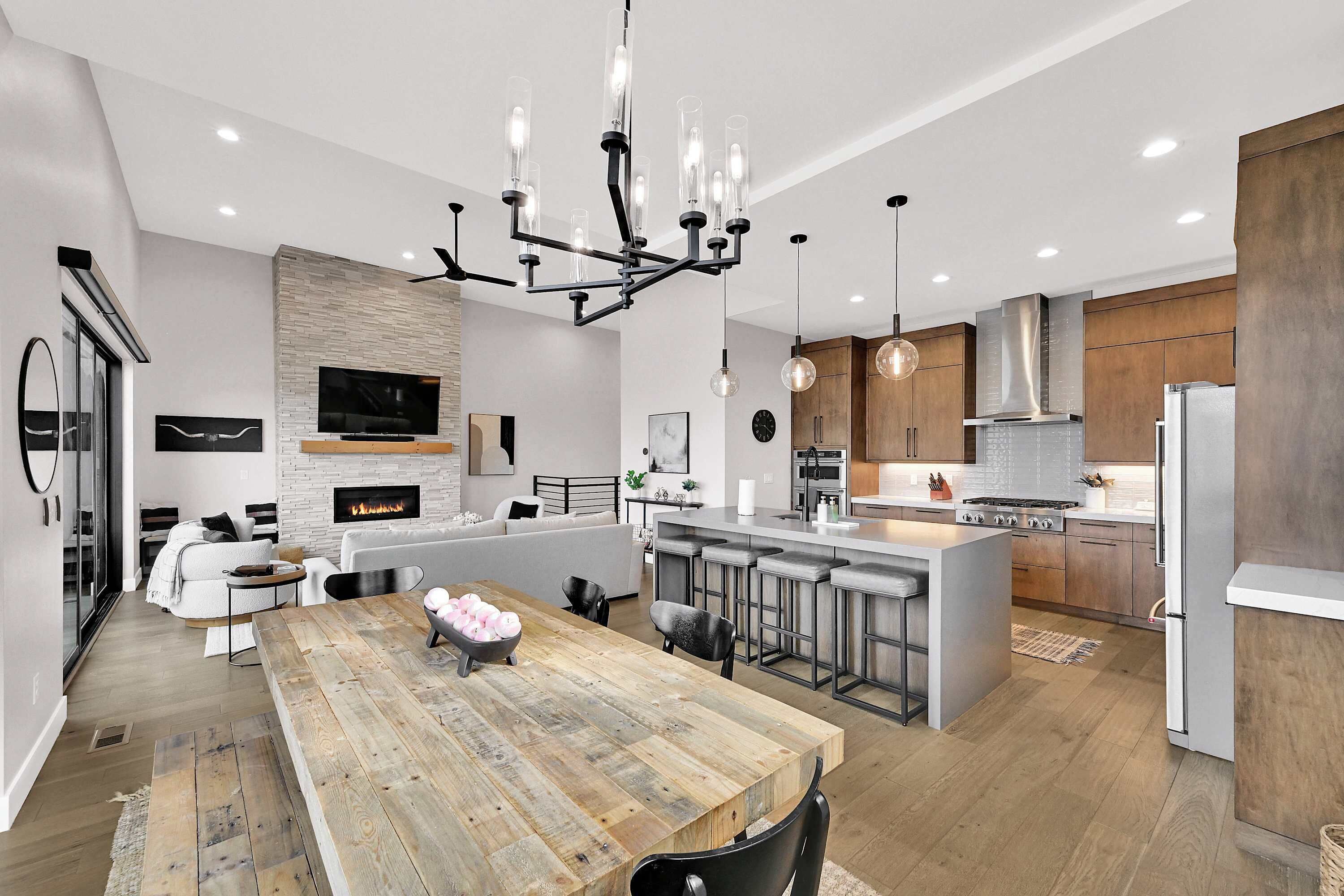 A modern kitchen with a central island, bar stools, a fireplace, and a dining area with a wooden table.