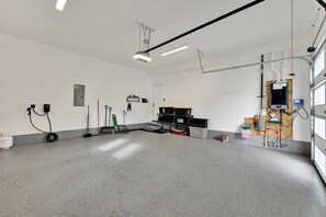 A clean, well-lit garage with a concrete floor, various tools, and equipment on shelves, and a door leading to a workshop area.