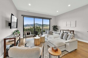 A modern living room with a large window, a sofa set, a coffee table, and a TV mounted on the wall. - 3BR Park City View Home | Hot Tub | Pet-Friendly (Hideout)