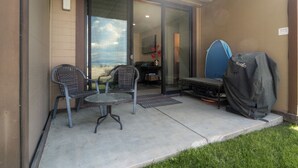 Un patio al aire libre con dos sillas de mimbre, una mesa redonda pequeña y una parrilla cubierta.