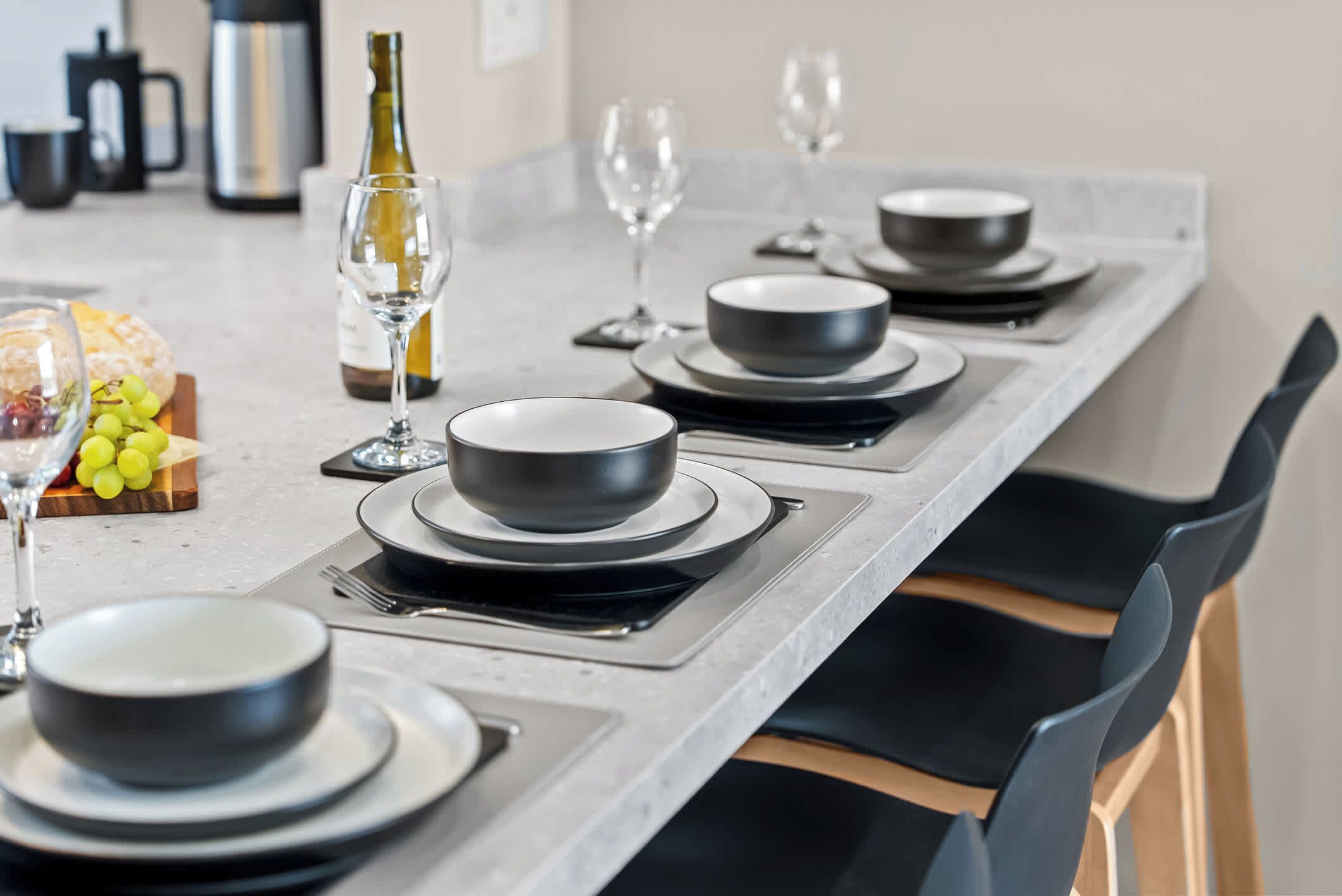 Una cocina moderna con una encimera amplia, platos negros, tazones y una botella de vino.