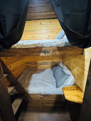 Een houten hutje met een stapelbed, een houten ladder en een klein tafeltje.
