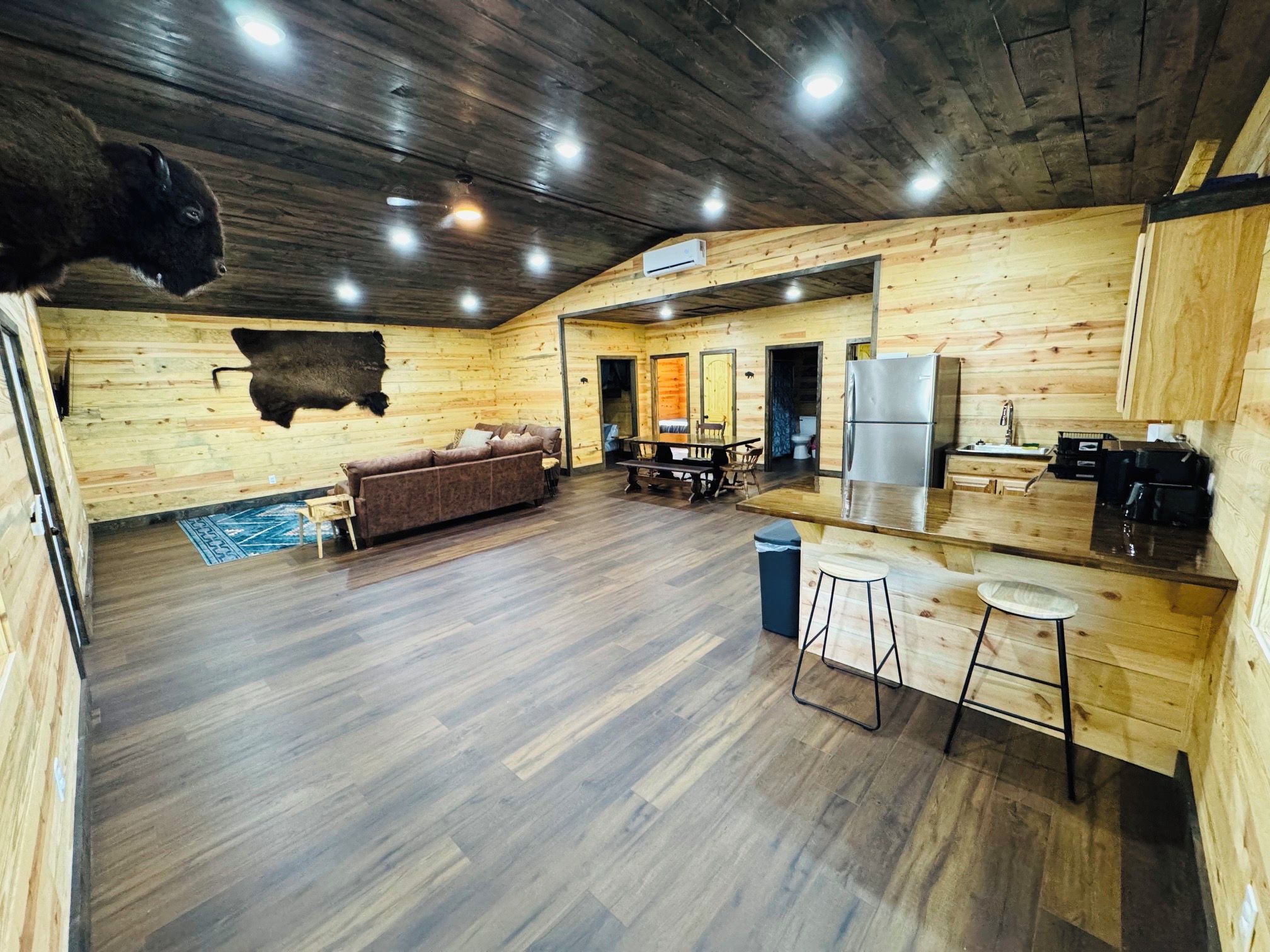 A log cabin interior with a living area, kitchen, and a large buffalo mounted on the wall.