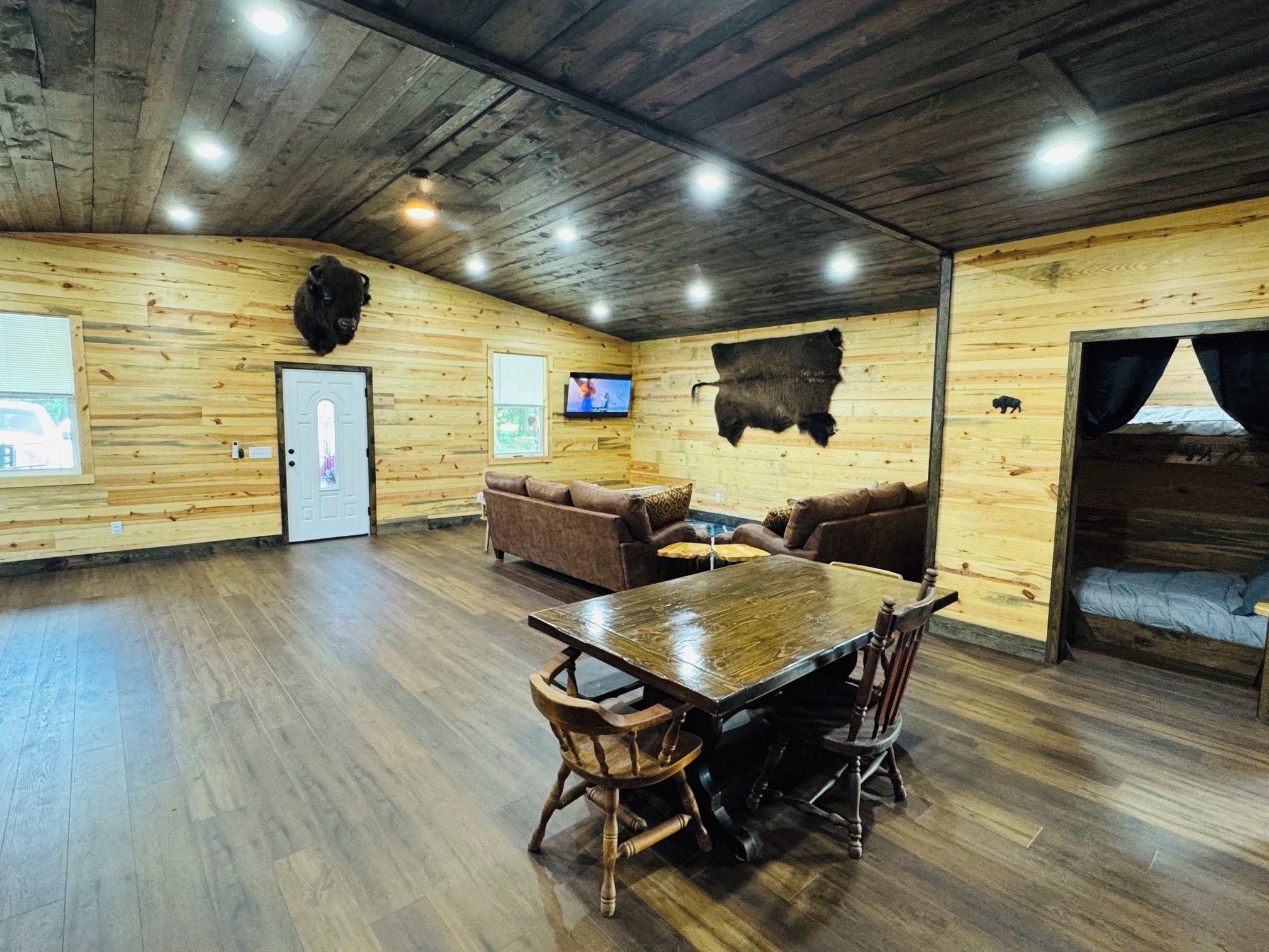 A spacious room with a wooden floor, a large table, and a television mounted on the wall.