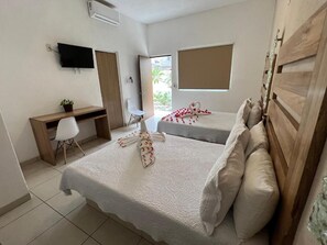 A hotel room with two beds, a desk, a chair, a TV, and a window. - Hotel y Condominios Jaroje (Crucecita)