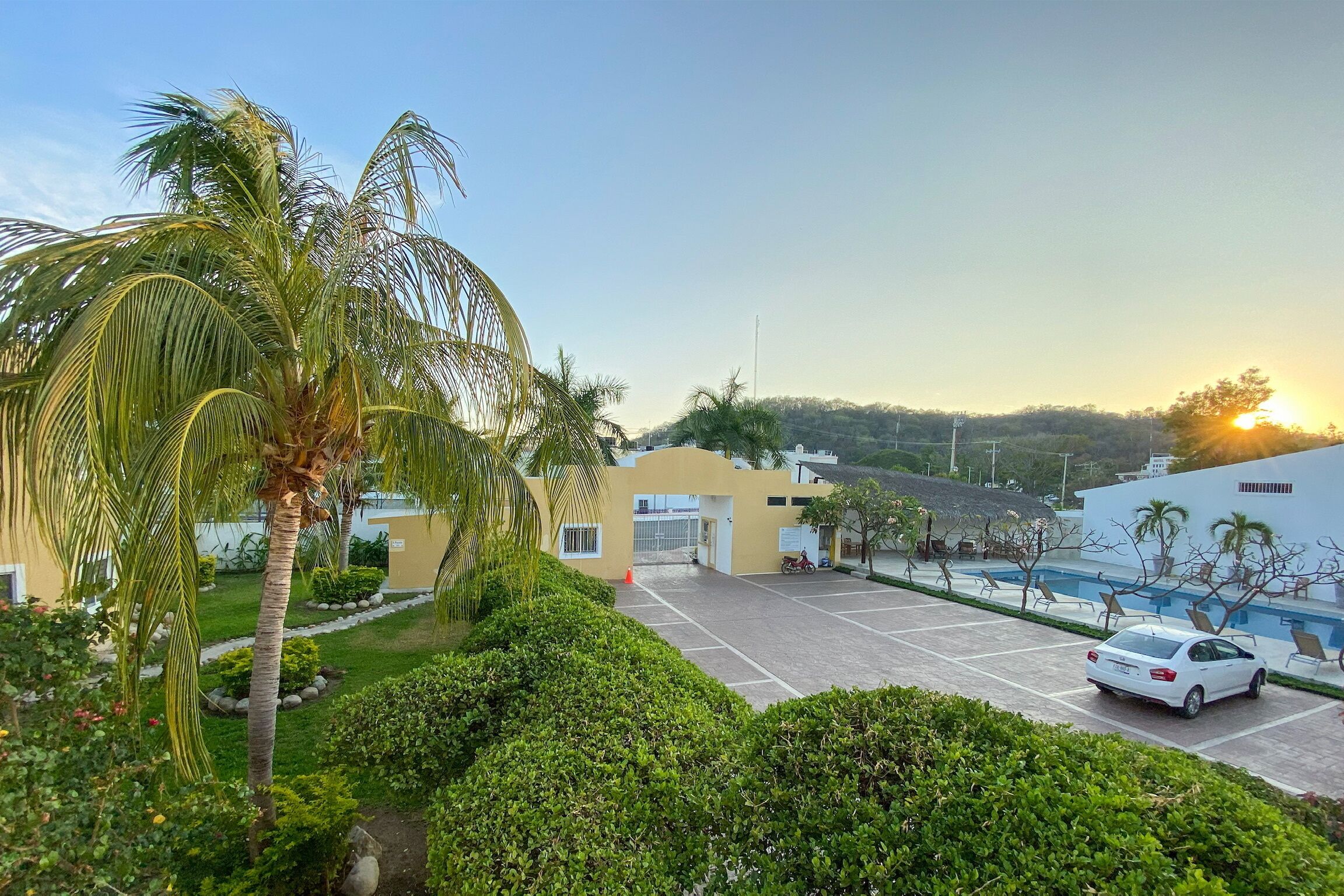 A hotel with a parking lot, a swimming pool, and a view of the sunset.