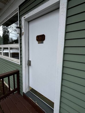 A white door with a number plate, a small sign below it, and a wooden railing in front. - Cozy 1-bedroom hotel room, Hamilton - 315 Chenango (Hamilton)