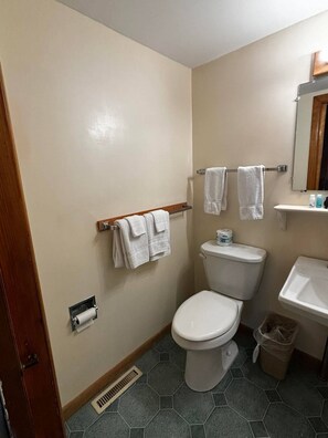 Un baño con inodoro, lavamanos, espejo y toallero.
