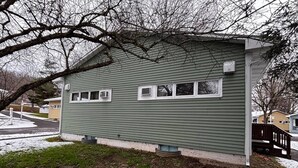 Una casa a un piano con facciata verde, un piccolo portico e una finestra ben visibile.