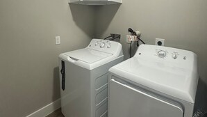 Uma lavanderia com duas máquinas de lavar e secar frontais brancas, um armário branco acima e uma ventilação no teto.
