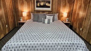 A room with wooden panel walls, a bed with patterned bedding, two bedside lamps, and a framed picture on the wall. - Private Lakefront Retreat - Fishing, Game Room - Lake Colorado City TX (Colorado City)
