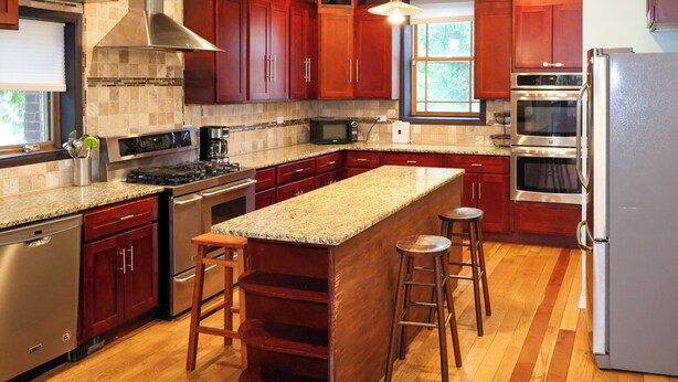 A kitchen with wooden cabinets, stainless steel appliances, a granite countertop, and a large island with stools. - Spacious 5-bedroom house in Chicago with AC Near Obama Center & UChicago (Chicago)