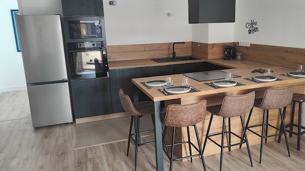 A modern kitchen with a central island, bar stools, a refrigerator, oven, and a coffee machine. - Premium Luxury Apartment (Dunkerque)