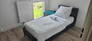 Una camera da letto con un letto, una finestra, un comodino e un termosifone.