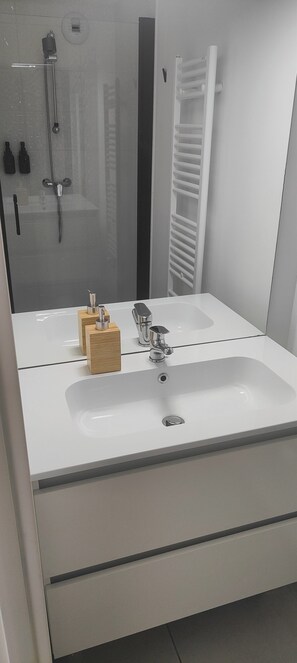 Un bagno moderno con un lavandino bianco, uno specchio e una doccia.