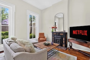 A living room with a sofa, armchair, coffee table, fireplace, and a television displaying 'NETFLIX'. - Relaxing home w/ poker lounge & spacious backyard! (Louisville)