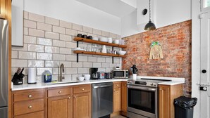 Eine moderne Küche mit Holzausstattung, einem Edelstahl-Geschirrspüler, einem Einbauofen und einer Küchenwand mit Backsteinverkleidung.