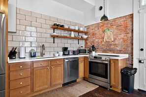 Eine moderne Küche mit Holzausstattung, einem Edelstahl-Geschirrspüler, einem Einbauofen und einer Küchenwand mit Backsteinverkleidung.