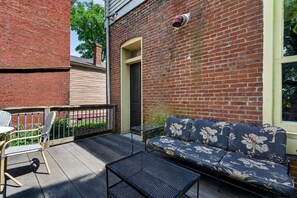A patio area with a brick wall, a sofa with floral upholstery, a metal table, and a chair. - Relaxing home w/ poker lounge & spacious backyard! (Louisville)