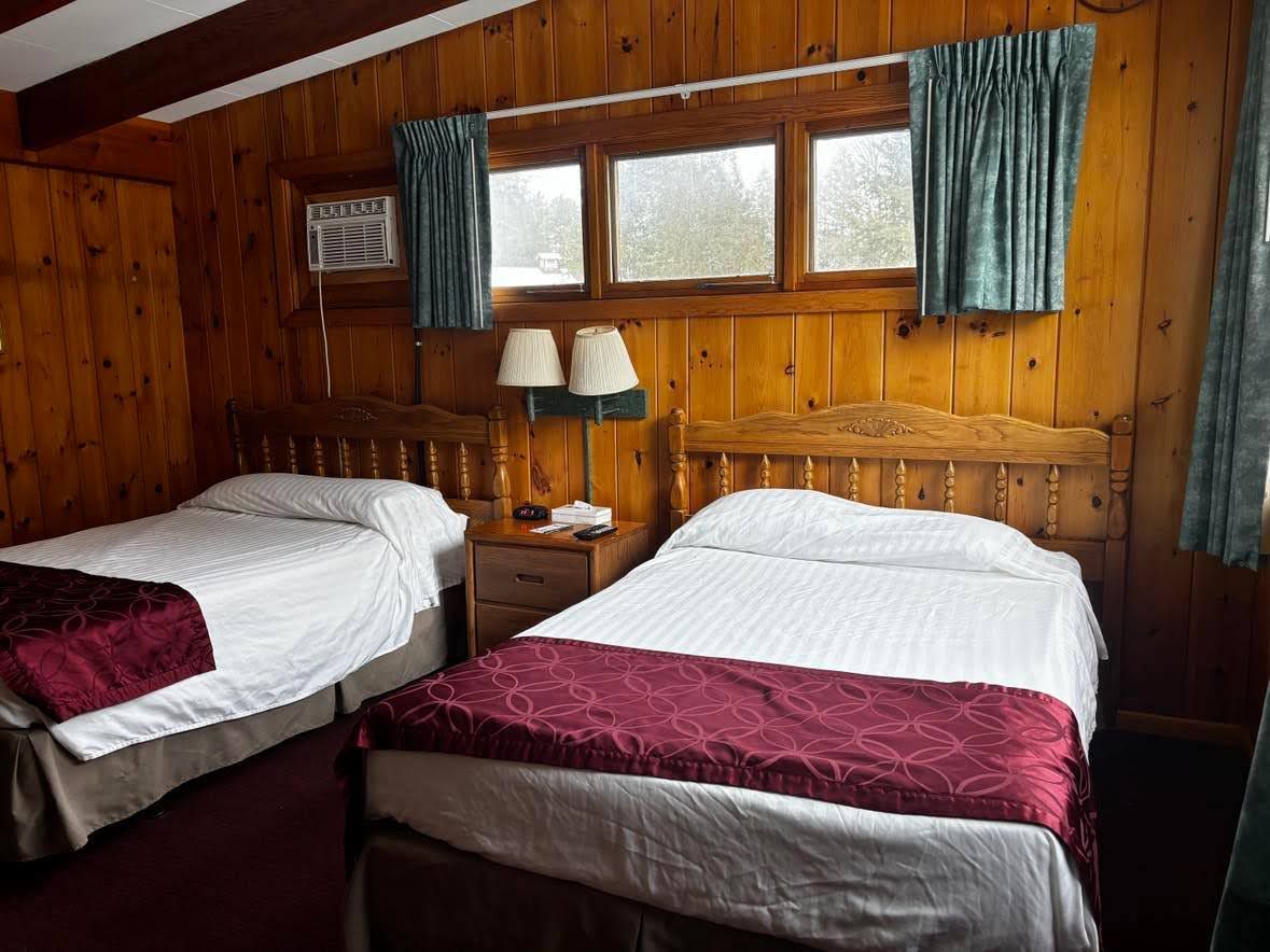 Una habitación con dos camas de madera, una mesita de noche con lámparas y un ventanal con cortinas.