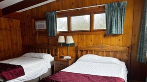 Une chambre avec deux lits en bois, une table de chevet avec des lampes et une fenêtre avec des rideaux.