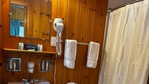 Une salle de bain avec un mur en bois, un lavabo blanc, des toilettes, un rideau de douche et un sèche-cheveux.