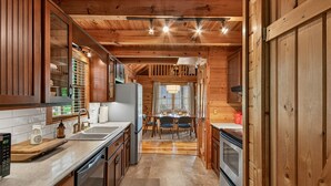 Interno di una baita in legno con angolo cottura, zona pranzo e vista sull'esterno.